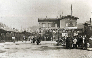 Empfangsgebäude vom Bahnhof Hamburg Klostertor; Passagiere mit Koffer / Handkarren. Im Hintergrund das Gebäude vom 1906 in Betrieb genommenen Hauptbahnhof.