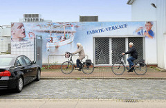 Leerstehendes Ladengeschäft, Fabrik Verkauf - Fassadenmalerei Fischkutter, Männer mit Fisch; FahrradfahrerIn in der Neufelder Straße von Cuxhaven.