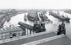 Historische Hafenansicht von Hamburg - Blick auf den Baakenhafen, lks. der Versmannkai und die Bögen der Pfeilerbahnstrecke - re.  Lagerschuppen und  Frachtschiffe am Petersenkai. Im Flusslauf der Norderelbe liegen Frachtsegler und Frachter an den
