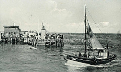 Ein Fischkutter läuft in den Hafen von Cuxhaven ein - Paddelboot auf dem Wasser; Holzsteg mit Schaulustigen an der Alten Liebe - Signalfeuer der Hafeneinfahrt.