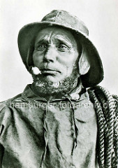 Historische Fotografie - Portrait eines Fischers in Ölzeug mit Pfeife und Bart - Tau über der Schulter.