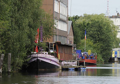 Auf dem Veringkanal liegen bunte Hausboote - die Uferzone ist dicht mit Weiden und Erlen bewachsen; im Hintergrund ist die Spitze des Hamburger Fernsehturms zu erkennen.
