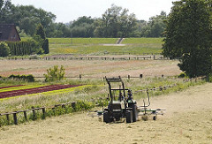 Ein Trecker wendet auf einer Wiese in Hambur Moorwerder das trockene Gras und bereitet es zur Heuernte vor.
