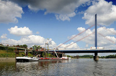 An der Anlegestelle Georgswerder liegt ein Tankschiff und wird über ein Schlauchsystem entladen. Autobahnbrücke mit Polygon und Seile.