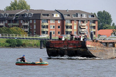 Ein Schubleichter wird von einem Schubschiff über die Billwerder Bucht gefahren; zwei Schiffer stehen am Bug des Schiffs und beobachten das kleine Schlauchboot.