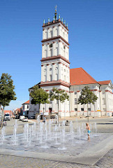 Springbrunnen am Marktplatz von Neustrelitz - Blick auf die Stadtkirche, die ursprünglich 1778 nach Plänen des Hofarztes Johann Christian Wilhelm Verpoorten errichtet wurde.