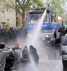 Eine Straßenblockade wird bei einer Demonstration in der Freien und Hansestadt Hamburg mit Hilfe eines Wasserwerfers aufgelöst. Mit Helm geschützte Fotografen fotografieren.