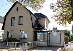 Wohnhaus mit  Mansarddach und gelber Klinkerfassade,  angeschlossenem ehemaligen Ladengeschäft für Milch  und Feinkost.
