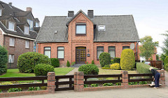 Einzelhaus in historischer Backsteinarchitektur mit Dachgiebel über dem Eingang; Ziegelpfeiler mit Holzzaun.
