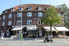 Halbrundes Backsteingebäude, Architektur der 1930er Jahre; Kaffee und kleine Bäckerei mit Sitzplätzen in der Sonne.
