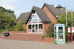 Moderne Architektur  der 1970er Jahre / Dorfhaus, Rathaus von Maschen - auf dem Dach die alte Uhr Schule. Rechts eine alte Telefonzelle, die als öffentlicher Bücherschrank genutzt wird.