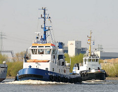 Die beiden Schlepper FAIRPLAY VI und HANS fahren auf dem Reiherstieg, um ein dort abfahrbereites Frachtschiff   zu schleppen.