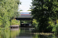 Blick vom Ernst-August-Kanal zur Mündung der Wilhelmsburger Dove-Elbe; ein Zug fährt über die Eisenbahnbrücke.
