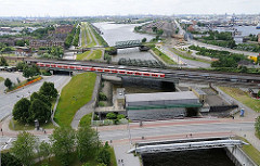 Im Vordergrund hinter der Wilhelmsburger Brücke das Müggenburger Sperrwerk und die S-Bahnstation Veddel - ein roter S-Bahnzug steht an der Haltestelle.