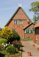 Bauernhaus mit Fachwerkgiebel in Hamburg Stillhorn; im Vorgarten blühen Pfingstrosen, die Fensterrahmen sind in regionaltypischem Grün gestrichen.