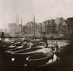 Historische Fotografie vom Hamburger Binnenhafen; Ewerführer stehen auf ihren Booten; im Hintergrund die Masten der Segelschiffe.