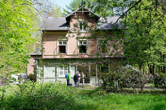 Außenansicht der unter Denkmalschutz stehenden  Villa Mutzenbecher, blühender Rhododendron vor der Holzveranda.
