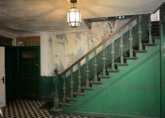 Treppe in der historischen Villa Mutzenbecher, eine alte Lampe beleuchtet den Raum - alter gedrechselter Antrittspfosten und Treppendocken im Stil der Gründerzeit.