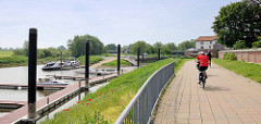 Hafenpromenade mit Radfahrern in Hitzacker; einige Sportboote liegen am Steg der Marina.