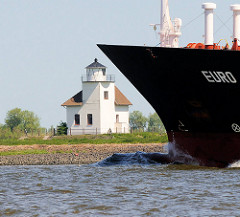Bug eines Frachtschiffs auf der Elbe - an Land der 1896 gebaute Leuchtturm Julesand in der Sonne.