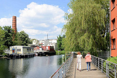 Fussweg über dem Wasser des Veringkanals in Hamburg Wilhelmsburg - im Hintergrund Hausboote, Arbeitsboot bei der Honigfabrik.