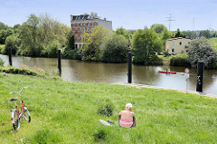 Sommertag in Hamburg Wilhelmsburg - Menschen im grünen Gras vom Deich am Ernst August Kanal - ein rotes Kanu fährt auf dem Wasser.