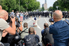 Fotografen bei der Arbeit beim Protest gegen den G 20 Gipfel in Hamburg, eine Demonstrantin sitzt alleine vor einer Polizeikette und hebt die Arme.
