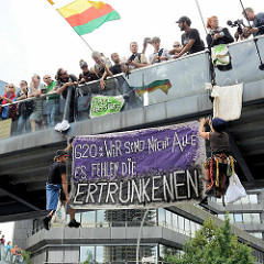 Zwei Demonstrant*innen haben sich von einer Fussgängerbrücke abgeseilt und ein Transpartent aufgehängt: G20: Wir sind nicht alle, es fehlen die ERTRUNKENEN.