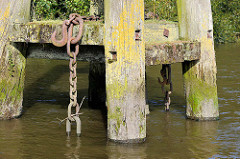 Holzdalben / Anlegepfähle aus Holz - Eisenketten hängen ins Hafenwasser; Prager Ufer im Moldauhafen, Hafenbecken im Hamburger Hafen.
