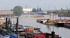 Arbeitsschiffe im Travehafen in Hamburg Steinwerder; ein Schubschiff mit Leichter fährt ein. Im Hintergrund das Polizeigebäude vom Wasserschutzpolizeikommissariat 2, Kirchtürme der Stadt + die Elbphilharmonie.