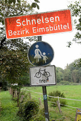 Stadtteil Grenze, Ortschild von Hamburg Schnelsen, Bezirk Eimsbüttel - Schild Fussweg, Fahrrad frei; Wiese mit Zaun.