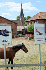 Pferd auf dem Weg zum Schuhkauf? Pferdekoppel mit Schuhwerbung im Dorfzentrum von Stelle.