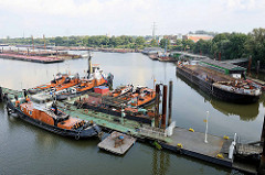 Übersicht vom Travehafen in der Hansestadt Hamburg - eine Wassertreppe führt zu einem Ponton mit Arbeitsschiffen - eine Schute liegt an einer Werftanlage.