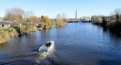Blick von einer Fussgängerbrücke am  Bullehuser Kanal; Schrebergärten / Kleingarten am Wasser mit Bootsteg; im Hintergrund Industrieanlagen in Hamburg Billbrook - ein Sportboot fährt Richtung Bille.