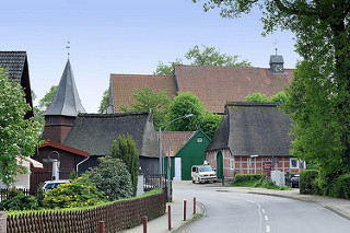 Blick durch die Bahnhofsstrße von Hittfeld zu historischen reetgedeckten Bauernhäuser und der Sankt Mauritiuskirche.