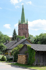 Kirchturm der Sankt Annen Kirche in Kuldīga / Lettland - erbaut 1904 - Architekt Wilhelm Neumann; Holzschuppen mit Feuerholz im Vordergrund.