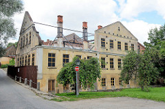 Historisches Gebäude am Alekšupīte-Bach in Kuldīga; das Dach ist abgerissen, die Fassade wird mit Eisenträgern gestützt.