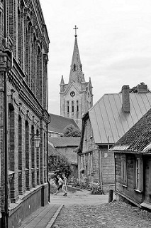 Altstadt von Cēsis, Lettland - historische Architektur, Strasse mit Kopfsteinpflaster - Kirchturm der Ende des 13. Jahrhundert erbauten St. Johanniskirche.