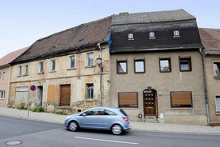 Wohnhäuser in Strehla - restauriertes Gebäude mit Rauhputz - leerstehendes Haus mit abgesprungenem Putz und vernageltem Fenster.