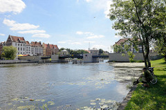 Ein Angler sitzt am Flussufer der Elbląg / Elbing - Neubauten am gegenüber liegenden Ufer.