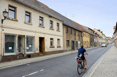 Leerstehende Wohnhäuser, Geschäfte in der Hauptstraße von Strehla, B 182 - Fahrradfahrerin mit Fahrradkorb.