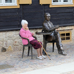 Bronzeskulptur in der Altstadt von Kuldīga / Lettland; sitzender Mann am Bistrotisch.