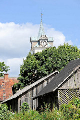 Holzschuppen und Kirchturm der Römisch-katholische Kirche der Heiligen Dreifaltigkeit in Kuldiga, Lettland.