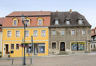 Wohnhäuser am Markt von Strehla - unterschiedliche Fassadengestaltung, frisch renoviert mit gelber Fassade und neu gedecktem Dach - grauer Rauhputz mit holzverkleideten Dachfenstern.