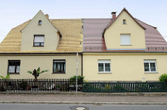 Doppelhaus in Schildau - symmetrische Wohnhäuser mit unterschiedlicher Dachdeckung und Vorgarten / Zaun.