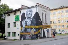 Fassadenmalerei - Bild auf einer Hausfassade in Tartu; Frau mit Strick + schwarzen Flügeln: Mrs REET / Streetartist - französicher Graffiti-Künstler MTO - Stencibility festival in April 2014.
