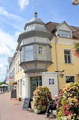 Sitzbank zwischen prunkvoll blühenden Blumentöpfen - Eckgebäude mit Erkerturm über dem Hauseingang; Nikolai / Pärnu.