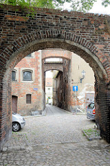 Schmale Gasse mit Ziegelmauer und gemauerten Hausstützen, Kopfsteinpflaster in Toruń.