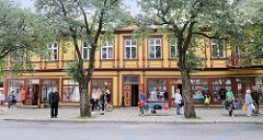 Geschäftshäuser mit Holzfassade - Fassade farbig abgesetzt; Menschen an der Bushaltestelle - Rüütli in Pärnu, Estland.
