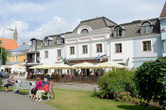 Grünanlage an der Munga in Pärnu - Sitzbänke in der Sonne; Café mit Terrasse unter Sonnenschirmen.